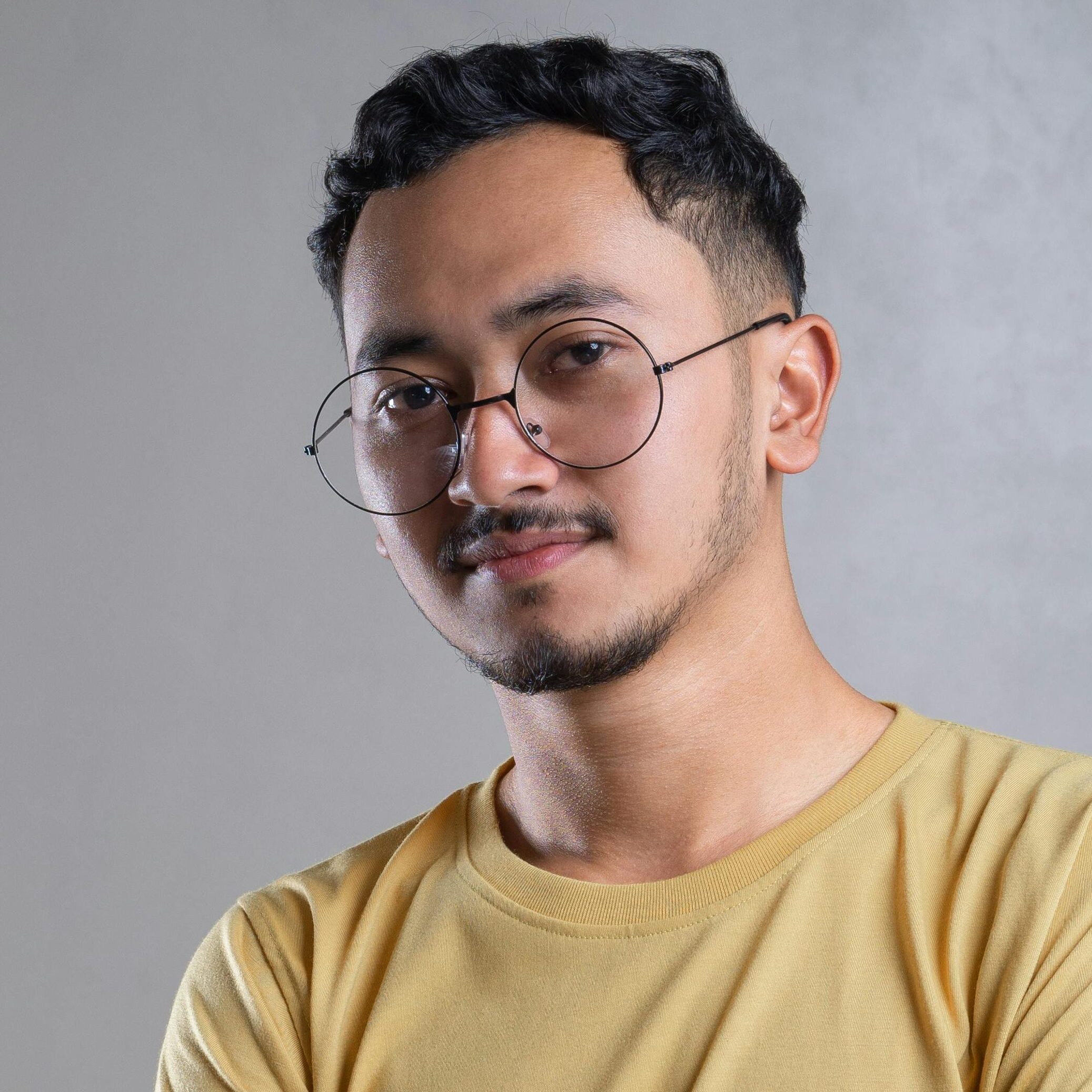 Portrait of a young man with eyeglasses and a confident pose in a neutral setting.
